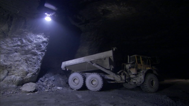 一辆自卸卡车在一盏顶灯的强光下将一车矿石倾倒在矿井里。视频下载