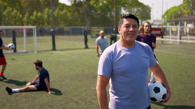 男足球运动员站在足球场上，手臂抱着球视频素材