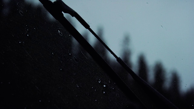 近距离慢动作拍摄的挡风玻璃雨刷清洗车辆的挡风玻璃上的雨，而驾驶附近的森林下的阴天在黄昏视频素材