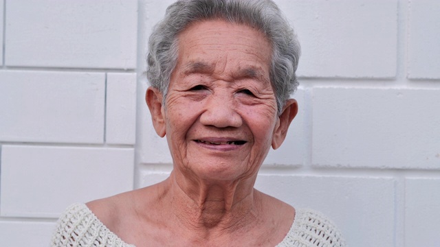 白色墙壁背景上微笑的亚洲老年妇女的肖像。肖像，老年人，退休，人，生活方式，医疗，保健和医学概念。高级的肖像视频下载
