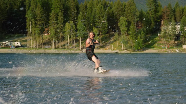 一个阳光明媚的下午，在蒙大拿维克多附近的格伦湖上，一个二十多岁的白人男子在滑水板上跳跃和表演特技视频素材