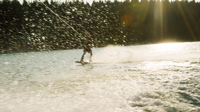 一个阳光明媚的下午，在蒙大拿维克多附近的格伦湖上，一个二十多岁的白人男子在滑水板上跳跃和表演特技视频下载