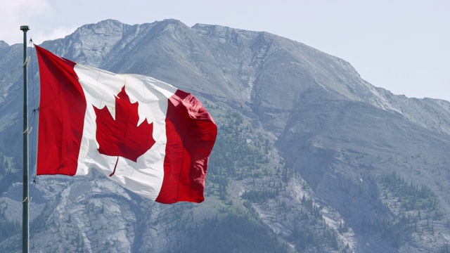 加拿大国旗在风中吹动的慢动作镜头与山在一个阳光明媚的日子的背景视频素材