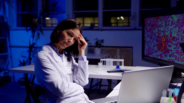 仰起疲惫的女科学家，脱下防护眼镜，坐在实验室书桌前看着笔记本电脑屏幕，想着测试结果视频素材