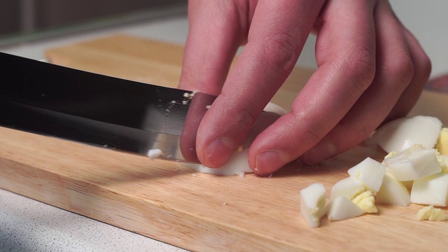 一名男子用一把大刀在厨房板上把煮熟的鸡蛋切成圆圈。家庭烹饪沙拉配料视频素材