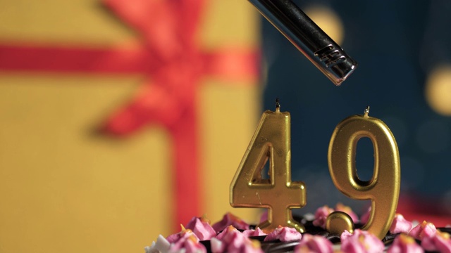 49号生日蛋糕用金色蜡烛点燃，蓝色背景的礼物用黄色礼盒系上红丝带。特写和慢动作视频下载