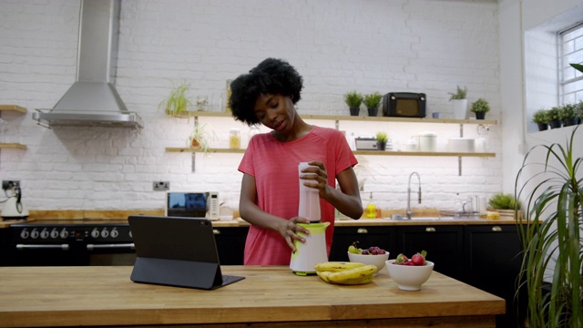 美丽的黑人妇女准备一个冰沙根据网上食谱平板电脑视频下载