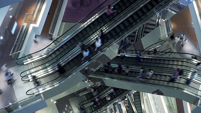 在大型现代购物中心，人们乘坐许多快速移动的自动扶梯。视频素材