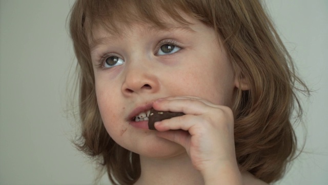 一个脏兮兮的有趣的3岁小女孩狼吞虎咽地吃着一块巧克力视频素材