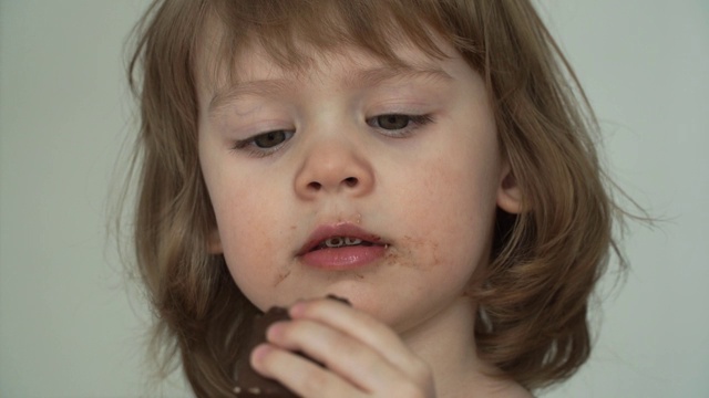 脏兮兮的3岁小女孩狼吞虎咽地吃着一块美味的巧克力糖视频素材