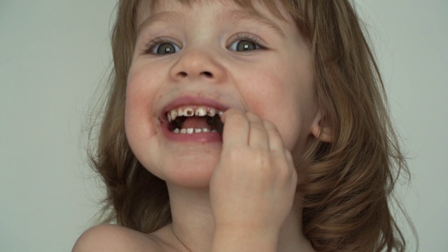 滑稽的3岁小女孩狼吞虎咽地吃着一块巧克力。Сhild被巧克力弄脏了。近距离视频素材