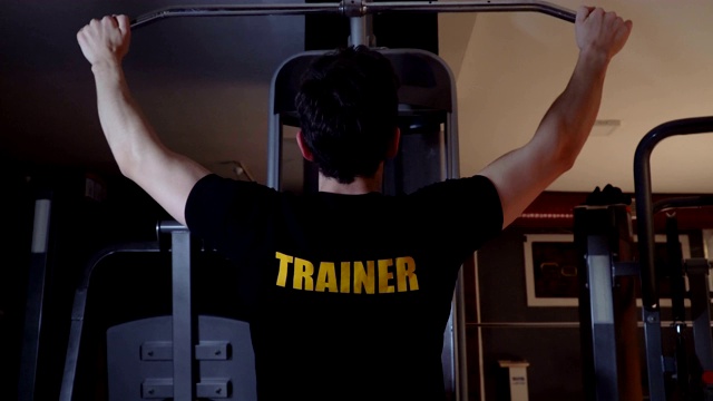 健身俱乐部的教练在侧拉式举重机上锻炼视频素材