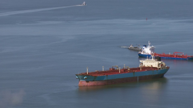 驳船和货船的鸟瞰图在墨西哥湾附近的加尔维斯顿湾和玻利瓦尔港与遥远的得克萨斯州城市。视频素材