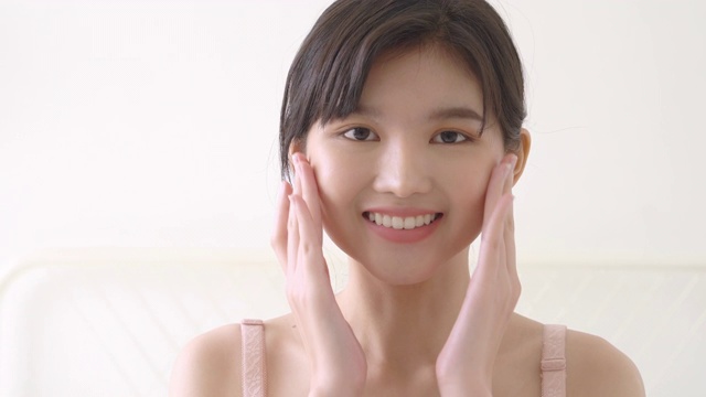 美丽年轻的亚洲女性化妆化妆品为面部柔软，女孩的手触摸面部光滑应用霜和护肤嫩肤，美丽完美的健康，皮肤护理和健康的概念。视频素材