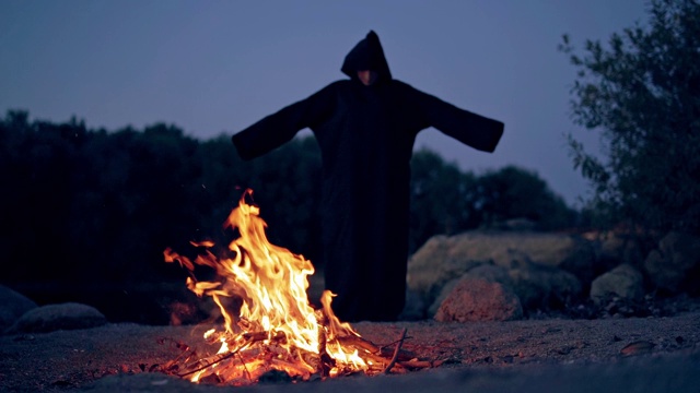 一个穿着黑色服装的恶魔在火旁的可怕景象。视频素材
