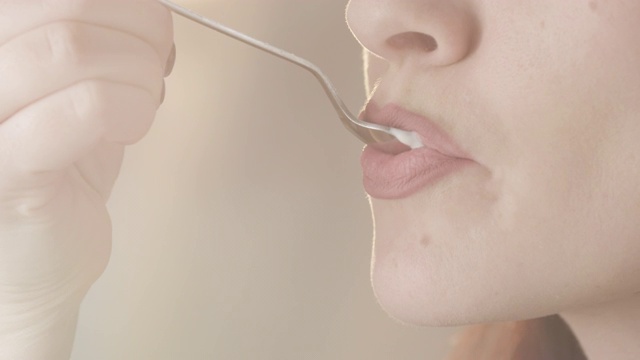 有吸引力的女性用勺子吃酸奶享受乳制品的味道口红和指甲的特写与模糊的背景与太阳闪光在红色上拍摄视频下载