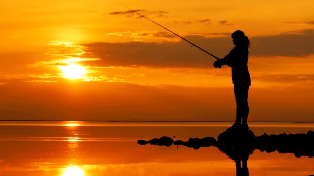 女人钓鱼在钓鱼杆旋转在夕阳的背景。视频素材