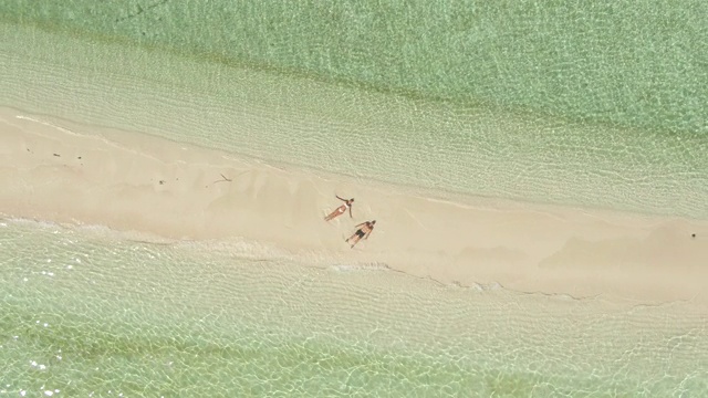 一名男子和一名女子在水上平房酒店度假村的一个沙洲热带岛屿上做一个雪天使无人机的视图。视频下载