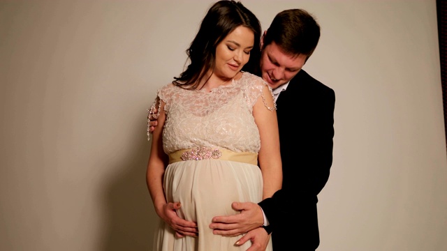 一个孕妇的肖像穿着晚礼服与丈夫在白色的背景视频下载