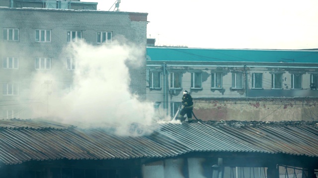 消防队员或消防队员在梯子上用烟扑灭公寓屋顶上燃烧的火焰视频素材
