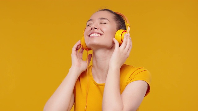 肖像的漂亮女孩听音乐通过耳机和舞蹈孤立在工作室黄色背景视频素材