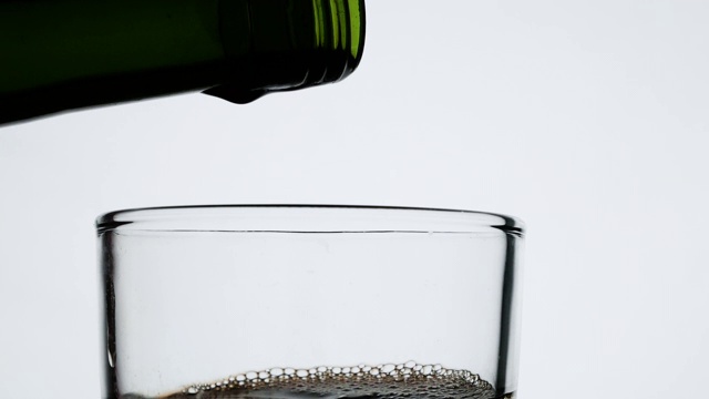 近距离倒果汁从绿色瓶子到玻璃，孤立在白色的背景。视频素材