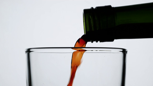 近距离倒果汁从绿色瓶子到玻璃，孤立在白色的背景。视频素材
