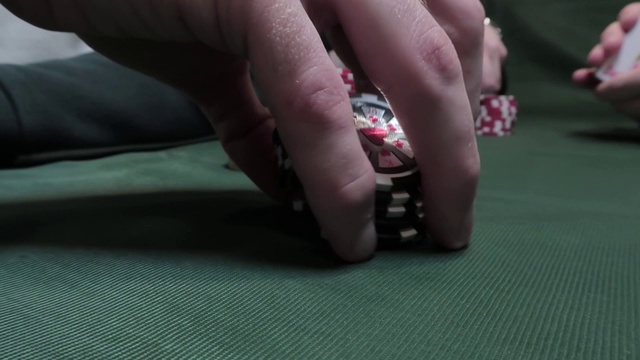 男性手使用扑克筹码在扑克桌上的特写，背景是绿色的布。休闲的概念视频素材