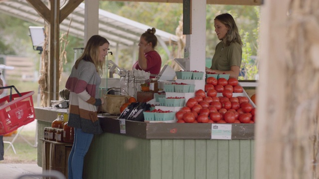 在农贸市场，一名年轻女子向收银员付款买了一篮蔬菜视频素材