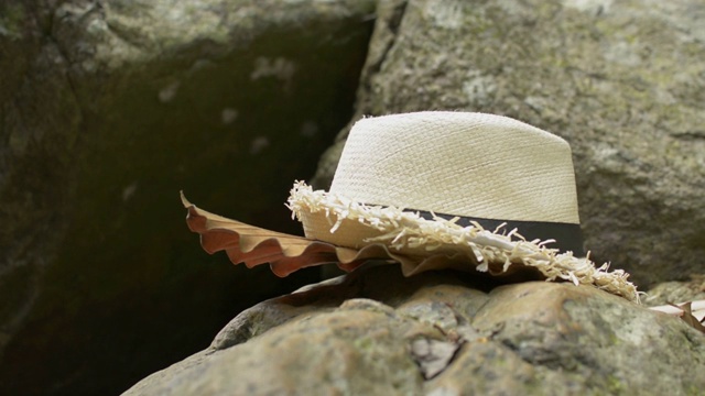 一个女人捡起一顶草帽，走在热带丛林的岩石上。视频下载