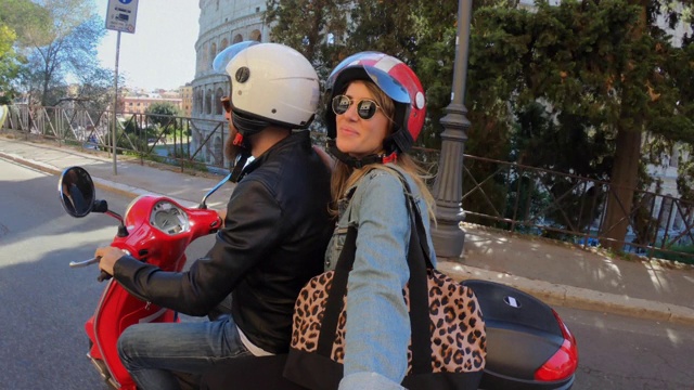 骑摩托车自拍:一对游客夫妇在体育馆旁骑摩托车视频下载