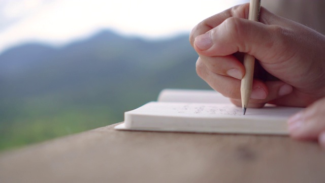 女性手写在白色笔记本上的4K视频，以工作空间美丽的自然风景为背景。视频素材