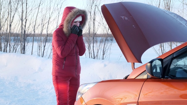 一个穿着红色冬季红色套装的女孩站在一辆破车旁。视频下载