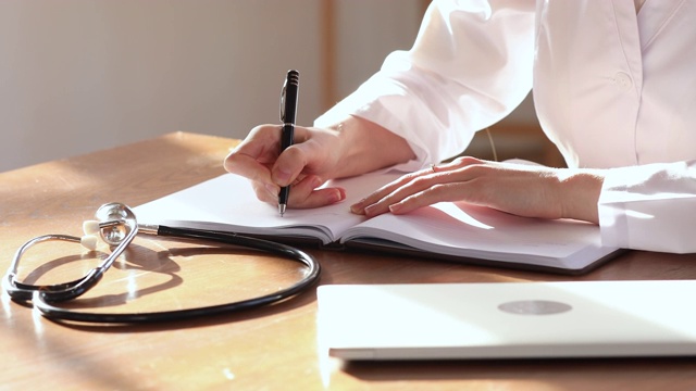 女医生穿白色制服在笔记本上做笔记，特写视频下载