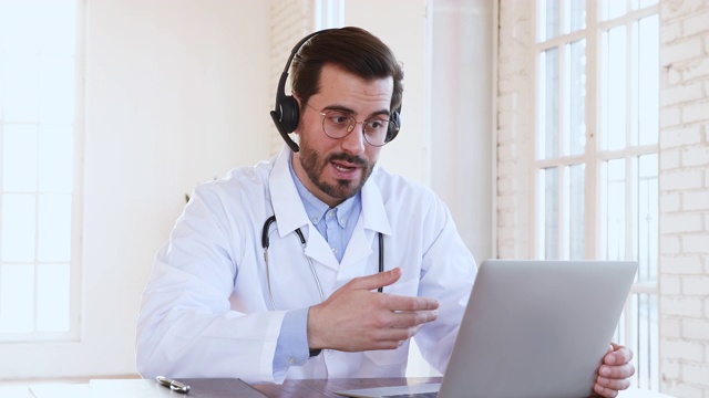 专业男医生戴着耳机在笔记本电脑上召开医疗电话会议视频下载