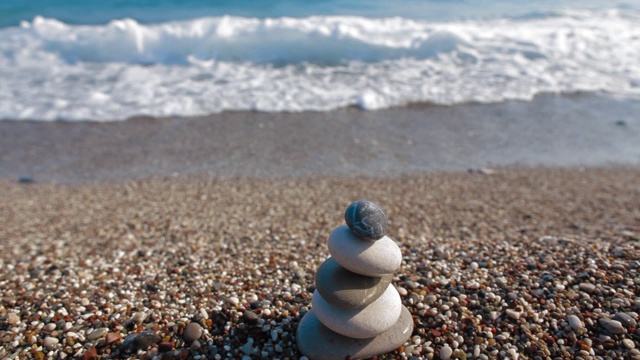 在海上堆积的圆形石头。光滑的小卵石堆在沙滩上，背景是蓝色平静的海水视频素材