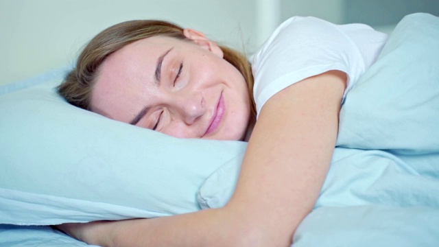 抱着柔软的白色枕头睡得很香的女人。少女休息，晚安睡眠的概念视频素材