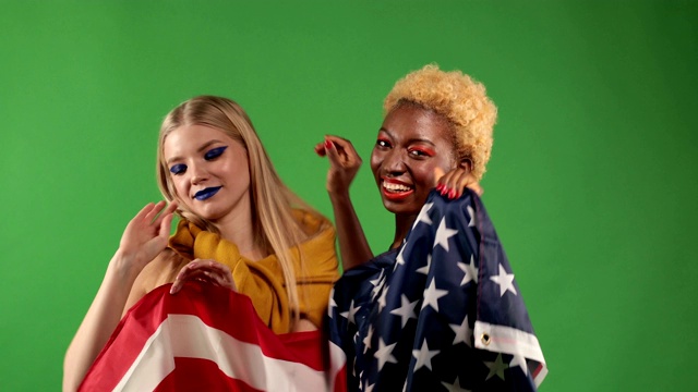 美丽快乐的女孩，白人欧洲和黑人非洲美丽性感年轻快乐的女孩跳舞与美国国旗在他们的手在独立日的荣誉视频下载