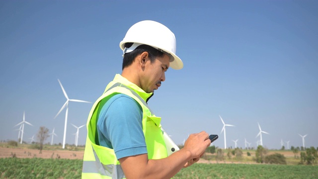 年轻工程师在风力涡轮机农场使用手机视频素材