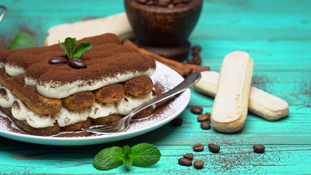 两份经典提拉米苏甜点和蓝色木质背景的萨瓦阿蒂饼干视频下载