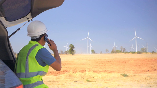 男性工程师使用智能手机在风力涡轮机农场工作视频素材