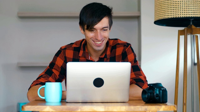 年轻男性摄影师用笔记本电脑处理图像，在家喝咖啡。视频素材