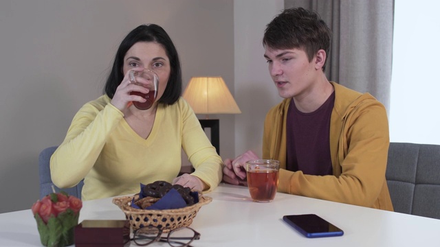 一个自信的白人少年和母亲坐在桌旁聊天。深色头发的成年女子一边喝茶，一边摇头表示不。沟通,生活方式、家庭。视频素材