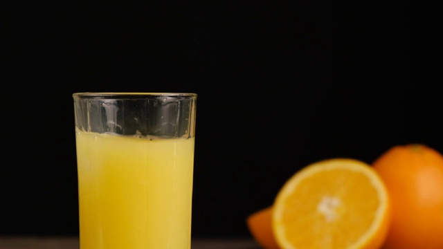 近距离的冰块落在玻璃杯的橙汁或柠檬汁与橘子在黑色的背景。用天然原料准备健康的早餐。缓慢的运动。视频素材
