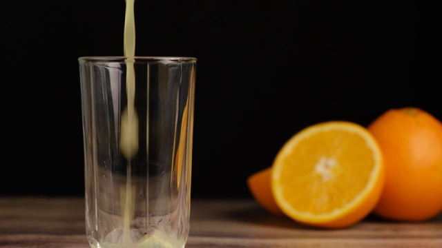新鲜的黄色果汁倒在木桌上，黑色背景上是橘子。自制水果橙汁，苏打水或柠檬水。有机维生素饮料。缓慢的运动。视频素材