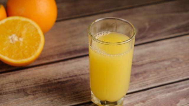 俯视图上的冰块落在橙汁或柠檬汁的玻璃杯和橘子木桌子上。用天然原料准备健康的早餐。缓慢的运动。视频素材