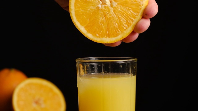 用手将橙汁挤出，倒进黑色背景的橘子玻璃杯中。用天然原料准备健康的早餐。缓慢的运动。视频素材