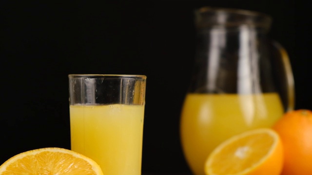 近距离的冰块落在橙汁或柠檬汁与橘子和水罐在黑色背景。用天然原料准备健康的早餐。慢动作视频素材