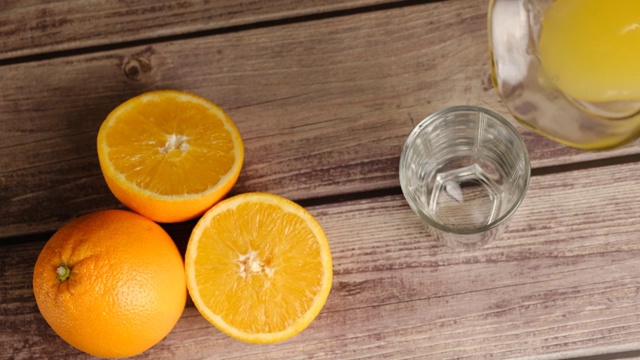 俯视图新鲜的黄色果汁从水罐在一个高脚杯倒在木桌上与橘子。自制水果橙汁，苏打水或柠檬水。有机维生素饮料。缓慢的运动。视频素材