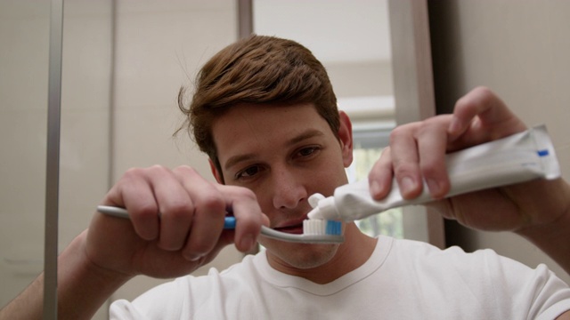 一个快乐的年轻人在家里一边刷牙一边看着镜头视频素材